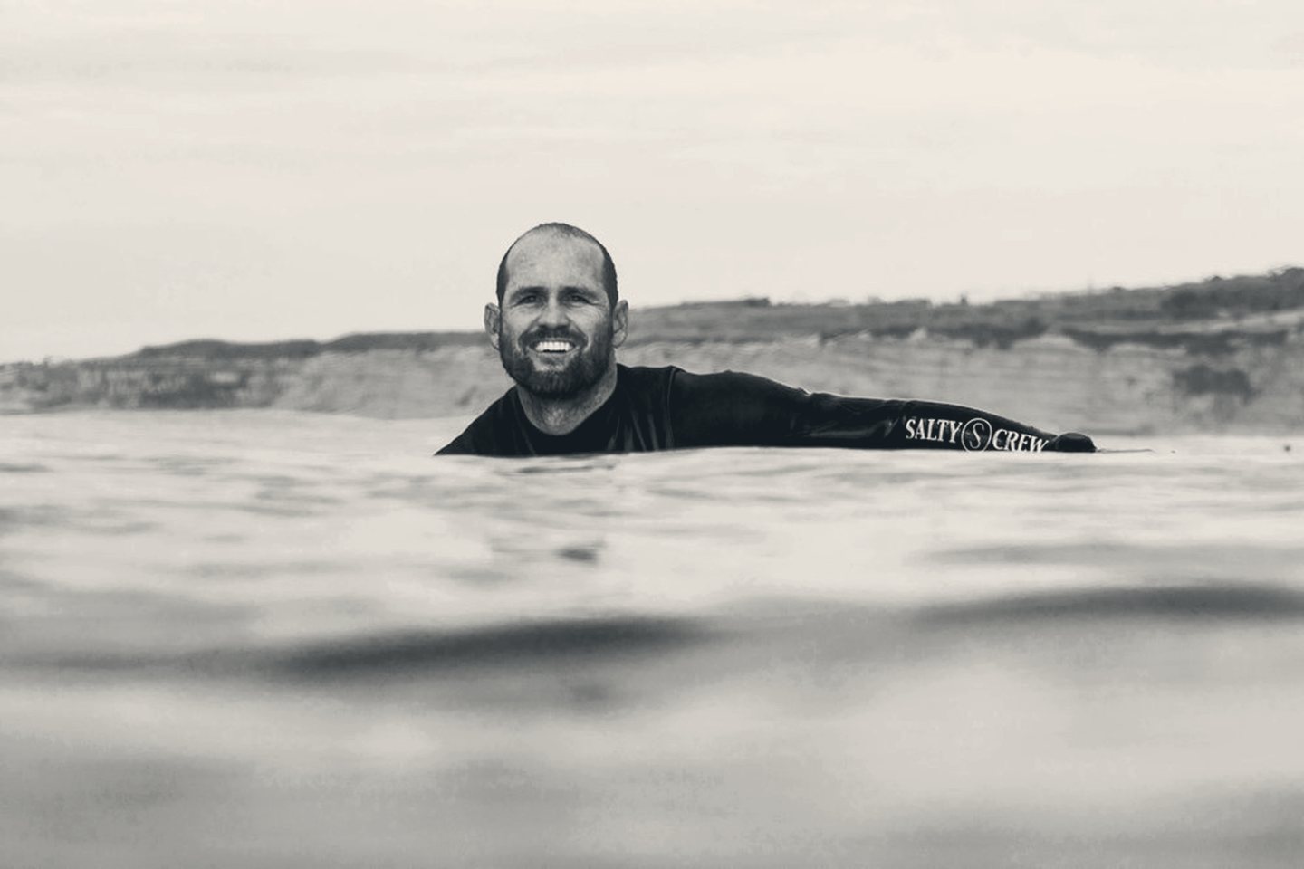 CJ Hobgood smiling in the lineup, arm resting on his board